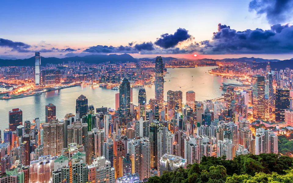 Aerial view of Hong Kong's skyline at sunset, with Victoria Harbour and Kowloon lit up in the background